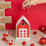 Casita navideña rellena de surtido Kinder, decorada con cinta roja y etiqueta Feliz Navidad